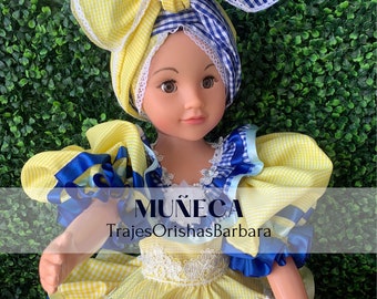May include: A yellow and blue doll wearing a yellow and blue checkered dress with a white lace trim. The doll is wearing a yellow and blue checkered head wrap with a blue bow. The doll is holding a blue ribbon in its hand. The text "MUÑECA TrajesOrishasBarbara" is printed on the doll's dress.