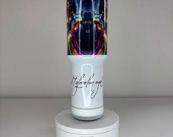 May include: A white cylindrical tumbler with a clear lid and a speaker base. The upper portion features a colorful, mirrored graphic of a person in vibrant clothing. The lower white section displays the black cursive text Maferefun Oya.