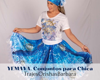 Op de afbeelding: Een vrouw draagt een wit T-shirt met een blauw en gouden ontwerp met de tekst "YEMAYA" en een blauw-witte rok met een witte kanten rand. De rok heeft een blauw-wit patroon met een nautisch thema. De vrouw draagt ook een blauw-wit hoofddoek. De tekst "YEMAYA. Conjuntos para Chica TrajesOrishasBarbara" staat onderaan de afbeelding.
