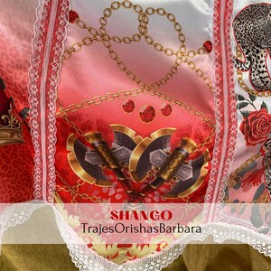 May include: A red, white, and gold fabric with a pattern of chains, axes, and roses. The fabric has a white lace trim and the text "SHANGO TrajesOrishasBarbara" is printed on the bottom.