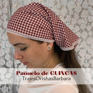 May include: A red and white gingham headscarf with white lace trim. The text "Pañuelo de GUINGAS" and "TrajesOrishasBarbara" is printed below the scarf.