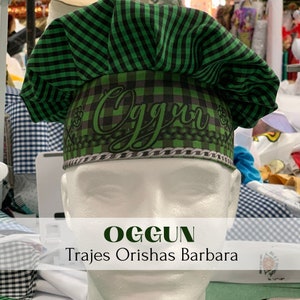 May include: A green and black checkered chef's hat with the word "OgguN" printed on it. The hat is on a white mannequin head. The text "OGGUN Trajes Orishas Barbara" is printed below the hat.