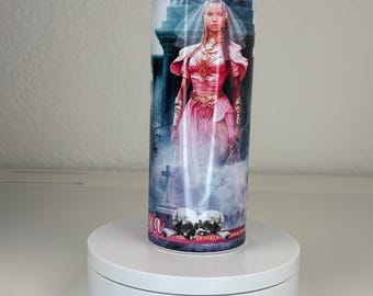 May include: A cylindrical tumbler featuring a graphic print of a person in a pink gown and veil standing in a graveyard setting with two skulls at the base. The design includes dark blue and purple tones, with the text "Lydia" visible near the bottom.