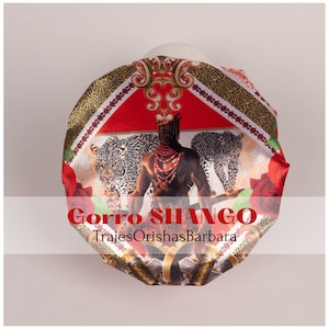 K&ouml;nnte beinhalten: Ein roter, schwarzer und goldener Satin-Kopftuch mit einem Aufdruck eines Mannes mit einer Krone, Leoparden und Rosen. Der Text "Gorra SHANGO" und "TrajesOrishasBarbara" ist auf dem Kopftuch aufgedruckt.