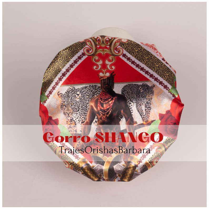 K&ouml;nnte beinhalten: Ein roter, schwarzer und goldener Satin-Kopftuch mit einem Aufdruck eines Mannes mit einer Krone, Leoparden und Rosen. Der Text "Gorra SHANGO" und "TrajesOrishasBarbara" ist auf dem Kopftuch aufgedruckt.