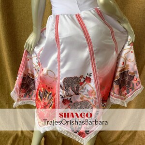 May include: White skirt with red and pink stripes and a print of leopards, roses, and drums. The skirt has a lace trim and the text "SHANGO TrajesOrishasBarbara" is printed on the bottom.