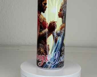 May include: A cylindrical tumbler featuring a vibrant graphic of a king and queen holding hands against a sunlit sky with a bird in flight. The design includes ornate gold and blue royal attire and the script text Virgo Year in red and blue.