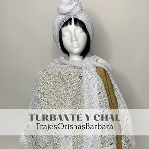 Może przedstawiać: Zestaw turbanu i szala z białej koronki. Turban jest zawiązany na szczycie głowy. Szal jest zarzucony na ramiona. Na szalu nadrukowany jest tekst "TURBANTE Y CHAL" i "TrajesOrishasBarbara".