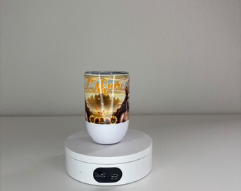May include: A white tumbler featuring a colorful graphic print of a figure with long dark hair, sunflowers, and butterflies, with the word Oshun written in a cursive orange font across the top section of the design against a sunset background.