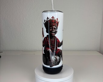 May include: A white cylindrical tumbler featuring a graphic print of a laughing child wearing a red crown and red beaded jewelry. The tumbler has a black base, a silver rim, and a clear plastic straw extending from the top, standing upright.