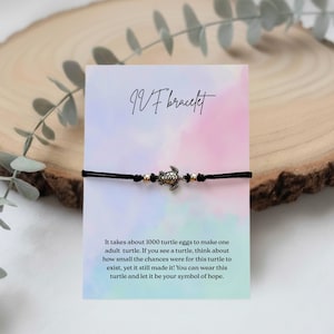 Könnte beinhalten: Schwarzes Armband mit einem Schildkrötenanhänger und goldfarbenen Perlen. Die Karte trägt die Aufschrift "IVF bracelet" und enthält einen inspirierenden Text über Schildkröten und Hoffnung. Auf Holzuntergrund.