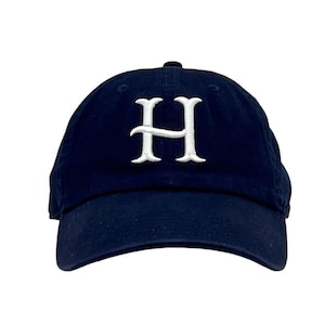 May include: Navy blue baseball cap with a white embroidered letter "H" on the front. The cap has a curved brim and an adjustable strap at the back. A classic and versatile accessory.