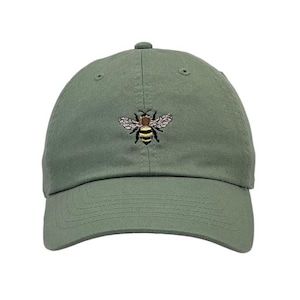 May include: Sage green baseball cap with a detailed embroidered bee design on the front. The cap has a curved brim and an adjustable strap at the back. A casual accessory for everyday wear.