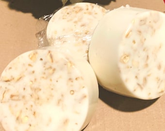 May include: Three round white soap bars with brown flecks. The soap bars are on a brown surface.