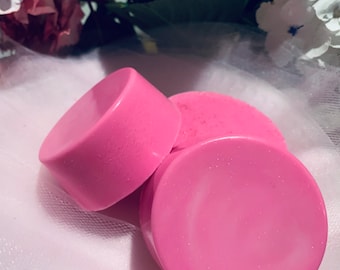 May include: Three pink round soap bars with a shimmery finish. The soap bars are stacked on top of each other.