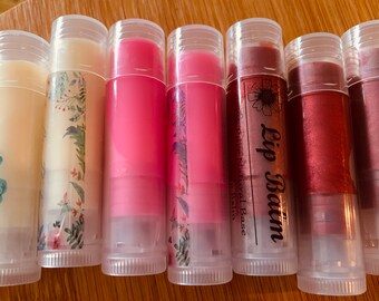 May include: Eight clear tubes of lip balm with different colored lip balms inside. The tubes have labels with floral designs and the text "Lip Balm Pure Natural Base Lip Balm".