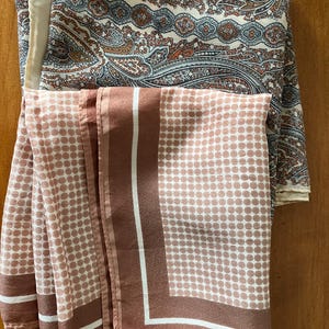 May include: A square scarf featuring two distinct patterns. The top section displays a detailed paisley design in shades of blue, cream, and rust orange. The bottom section features a dusty rose pink background with white polka dots and borders.