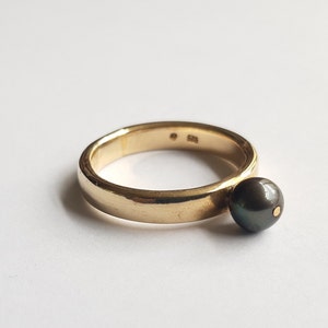 May include: A gold ring with a black pearl. The ring is simple and elegant, with a smooth band and a single pearl.