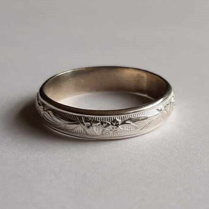 May include: A silver band ring with a floral design engraved around the entire band.