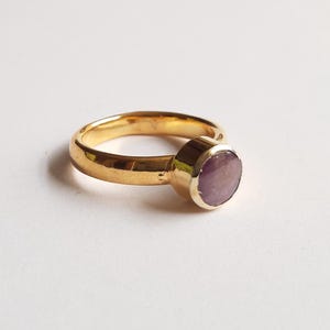 May include: A gold ring with a round, purple gemstone set in the center.