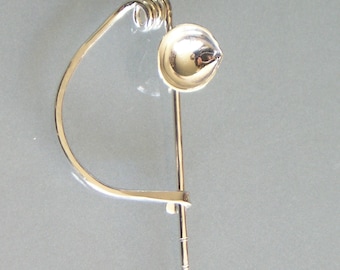 May include: A silver brooch with a curved, open design and a round, silver orb at the top. The orb is attached to the brooch by a thin, silver rod.