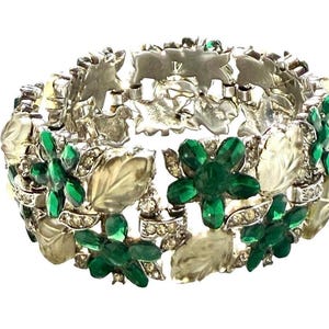 May include: A link bracelet featuring alternating floral motifs with deep green faceted stones and frosted clear glass leaves. The metal links are silver-toned and accented with small clear rhinestones, creating a continuous botanical pattern.