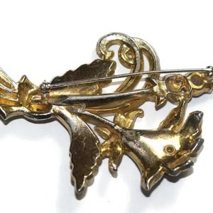 May include: Gold tone brooch with a floral design featuring a cluster of flowers with rhinestones. The brooch has a pin back.