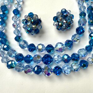 May include: A vintage jewellery set featuring a multi-strand beaded necklace and matching clip-on earrings. The beads are faceted and range in shades of blue, from light to deep sapphire, with iridescent accents. The earrings are clustered with similar beads.