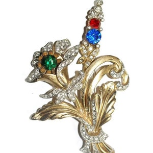 May include: A gold-toned brooch with a floral design. The brooch features a cluster of flowers with green, red, and blue rhinestones.