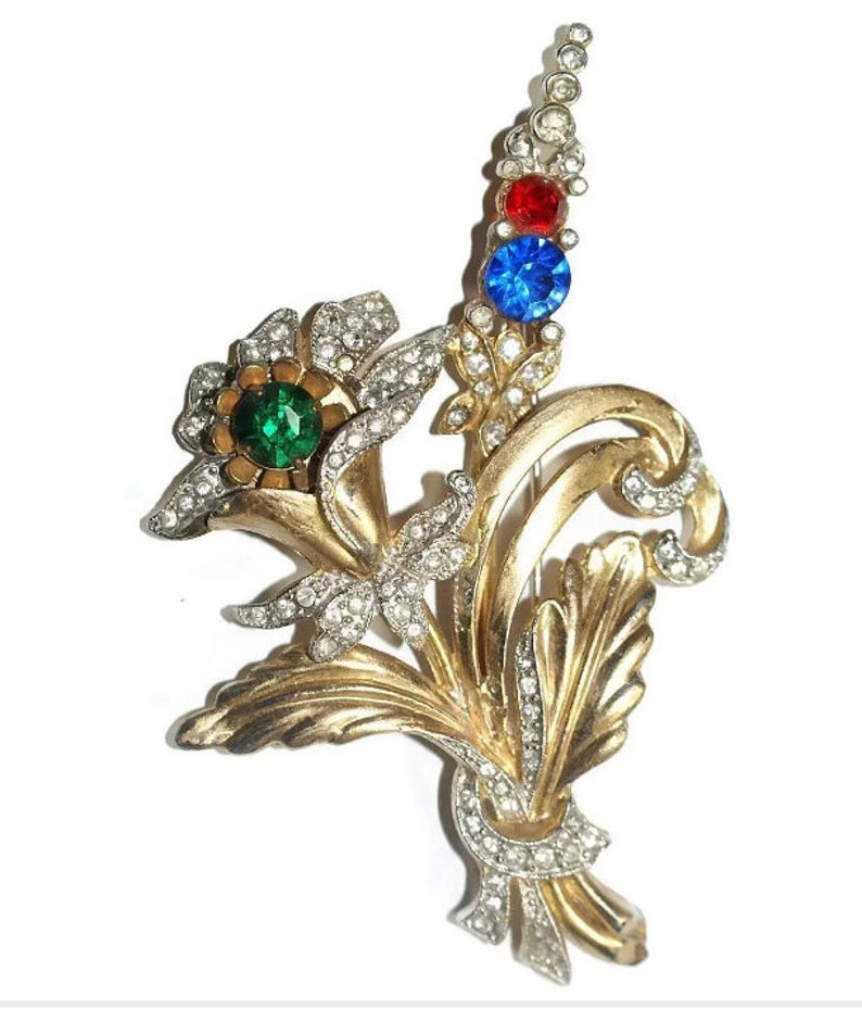 May include: A gold-toned brooch with a floral design. The brooch features a cluster of flowers with green, red, and blue rhinestones.