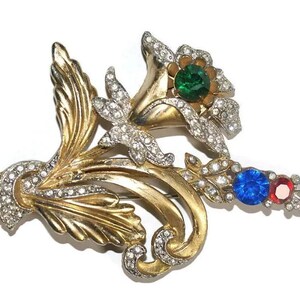 May include: A gold-tone brooch with a floral design featuring three large rhinestones in green, blue, and red.