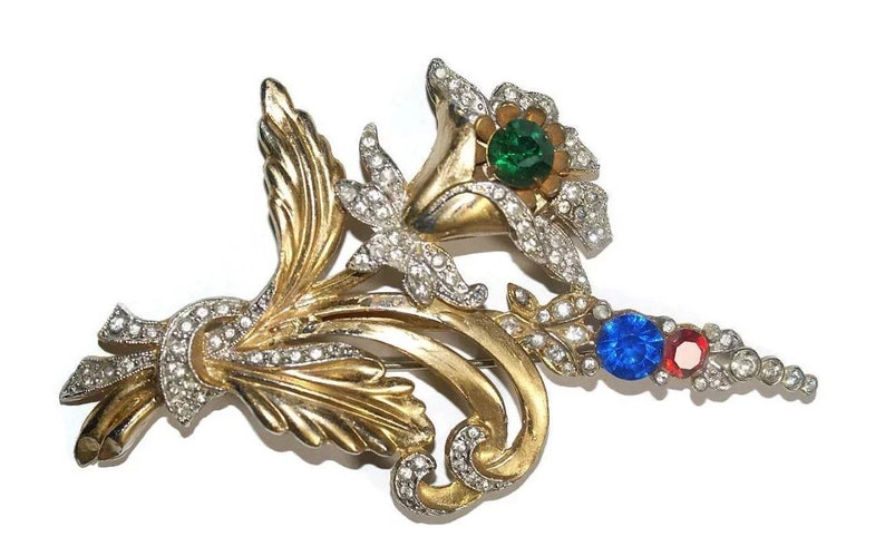 May include: A gold-tone brooch with a floral design featuring three large rhinestones in green, blue, and red.