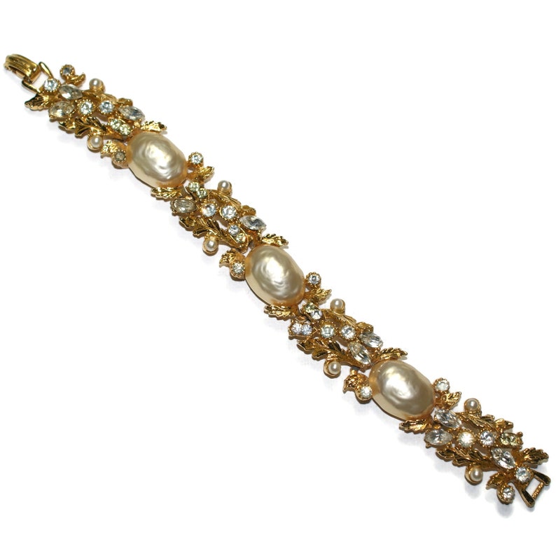 May include: A gold bracelet with faux pearls and clear rhinestones set in a floral design.