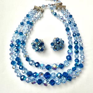 May include: A vintage jewellery set comprising a three-strand necklace and matching clip-on earrings. The necklace and earrings are made of faceted blue crystal beads in varying shades. The necklace has a silver-tone clasp.
