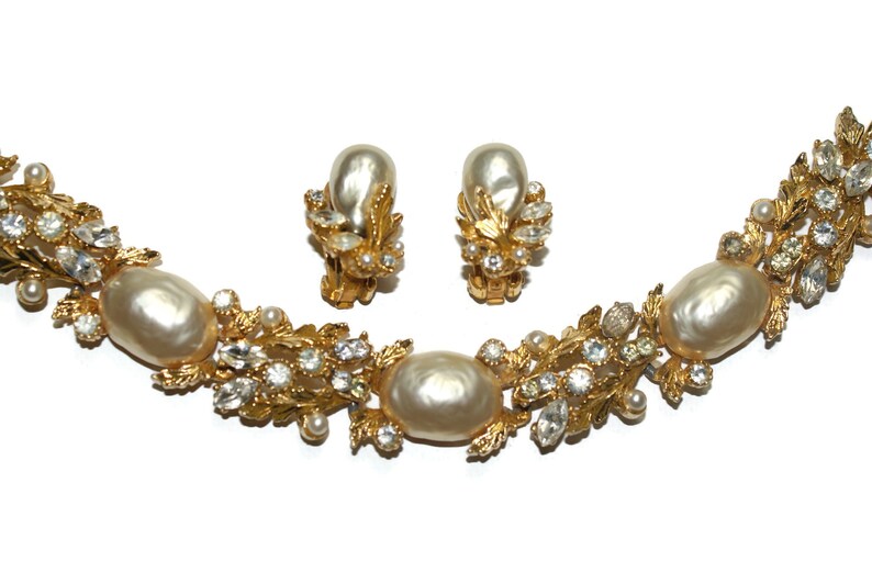 May include: A gold necklace and earrings set with faux pearls and rhinestones. The necklace features a delicate leaf design with faux pearls and rhinestones.