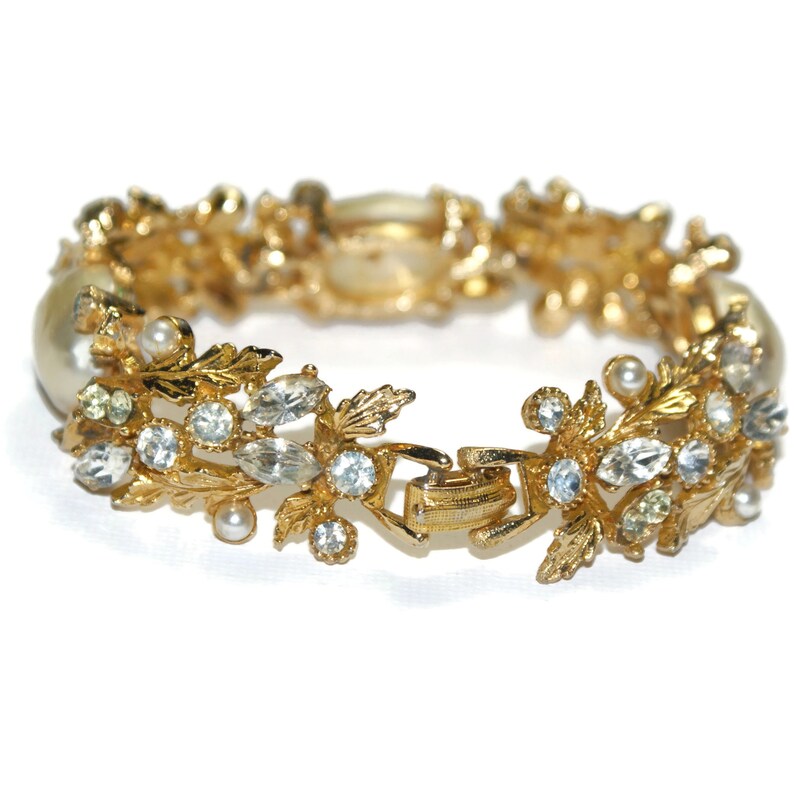 May include: A gold bracelet with a floral design featuring faux pearls and rhinestones.