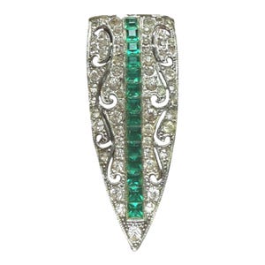 May include: A silver-toned Art Deco brooch, featuring a central line of emerald-green, square-cut stones. The brooch has a shield or teardrop shape, with clear, round-cut stones and decorative scrollwork along the edges.