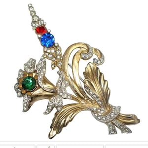 May include: A gold-toned brooch with a floral design. The brooch features a green, blue, and red rhinestone accents.
