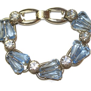 May include: A vintage bracelet featuring light blue, faceted glass stones and clear rhinestone accents. The bracelet has a silver-tone metal setting and a secure clasp. A classic piece of jewelry.