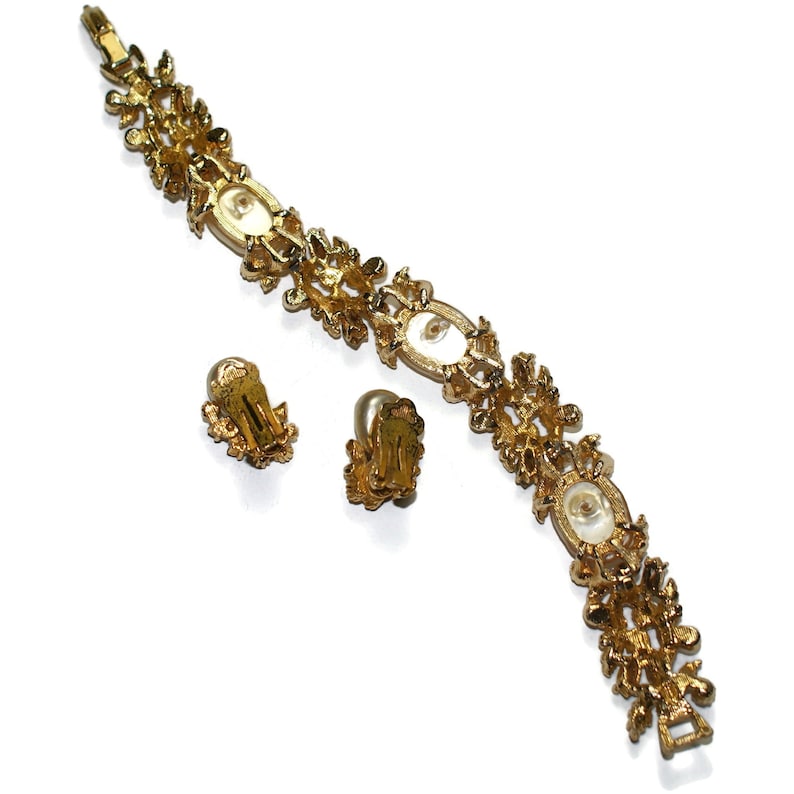 May include: A gold tone bracelet and matching clip-on earrings with faux pearl accents. The jewelry features a floral design.