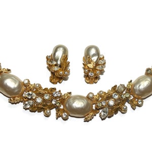 May include: A gold tone bracelet and earrings set with faux pearls and clear rhinestones. The jewelry features a floral design with leaves and small pearl accents.