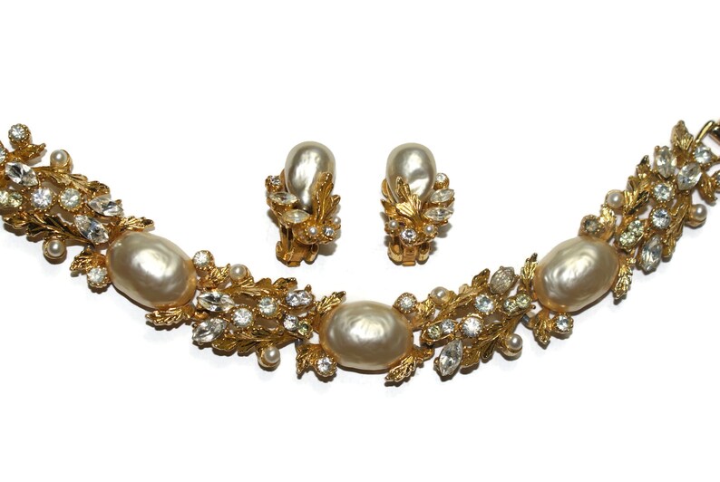 May include: A gold tone bracelet and earrings set with faux pearls and clear rhinestones. The jewelry features a floral design with leaves and small pearl accents.