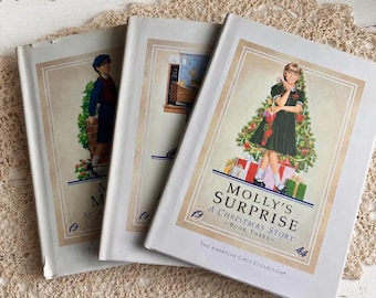 May include: Three hardcover books from The American Girls Collection. The front book is titled Molly's Surprise: A Christmas Story - Book Three, featuring an illustration of a girl in a green dress standing in front of a decorated Christmas tree.
