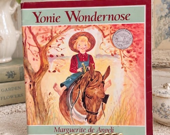 May include: A hardcover children's book titled Yonie Wondernose by Marguerite de Angeli. The cover features a watercolor illustration of a child with blonde hair wearing a straw hat and blue overalls, riding a brown horse under a tree.