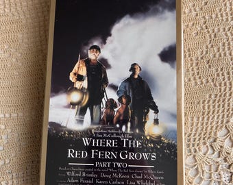 May include: A VHS tape case for the film Where The Red Fern Grows Part Two. The cover features two people and two dogs standing in a dark, misty landscape, each holding a glowing lantern. Text includes Family Classics, The Classic Continues, and cast names.