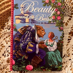 May include: A book cover with a blue background and a rose bush. The title is "Beauty and the Beast" by Madame le Prince de Beaumont. The illustration shows a beast in a blue and gold robe holding a woman's hand.