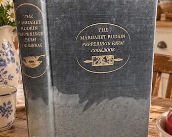 May include: A dark blue hardcover book titled The Margaret Rudkin Pepperidge Farm Cookbook. The cover features gold lettering, a gold rolling pin illustration, and a lighter blue textured section at the bottom. The spine also displays the title.