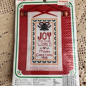 May include: A counted cross stitch kit featuring a Christmas design. The kit includes a banner with the words "JOY TO THE WORLD MERRY CHRISTMAS 1900" in cross-stitch. The packaging is red, white, and green, with a price tag of $122.