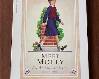 May include: A paperback book titled Meet Molly An American Girl Book One from The American Girls Collection. The cover features an illustration of a girl in a blue outfit and beret walking past a brick pillar. Scholastic 0-590-43785-2 is printed.