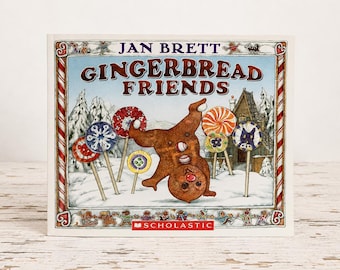 May include: A hardcover children's book titled Gingerbread Friends by Jan Brett. The cover features a brown gingerbread person doing a handstand in the snow, surrounded by colorful lollipops, a wooden house, and a red and white candy cane border.